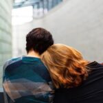 Photo of two people sitting. One person has her head on the other person's shoulder.